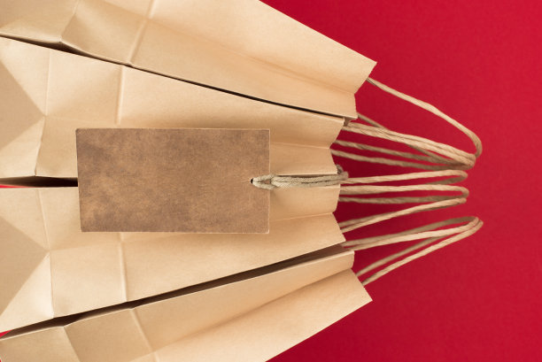 购物的概念。近距离照片的三个牛皮纸包装与纸板挂串徽章孤立在明亮的红色背景图片下载