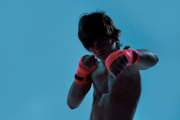 剪影拍摄的小男孩拳击手与拳击绷带在手上，看着摄像机，打击而站在孤立的蓝色背景图片下载