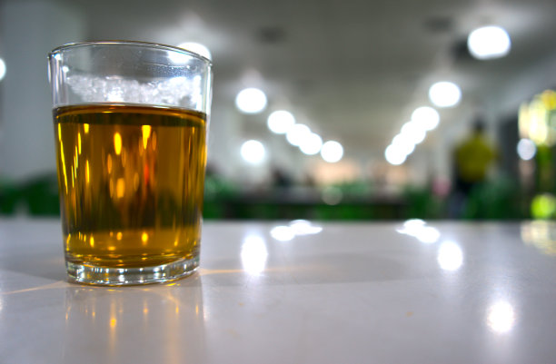 热茶饮以散焦为背景。饭堂、自助餐厅或餐厅桌上的装有金色清水饮料的圆筒玻璃杯。饮料、消费饮料、咖啡因等的概念。拍摄的。图片下载