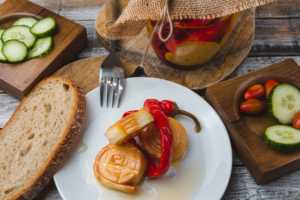 用橄榄油腌制的奶酪和辣椒放在玻璃罐中，叉子，盘子，西红柿面包和黄瓜在木头背景上。健美的照片图片下载