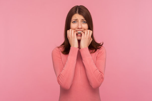 紧张困惑的深色头发的女人在粉红色的毛衣咬指甲在她的手指在恐慌，沮丧，悲伤图片下载