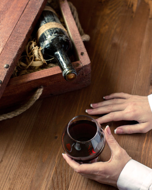 人的手拿着一杯红酒。旧瓶在复古木板条箱中间剃须，在木制背景上选焦点图片下载