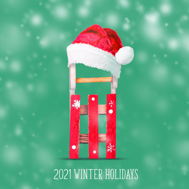 2021年冬季旅游。戴着圣诞老人帽的雪橇，在绿色的背景上。冬游概念，寒假。图片下载