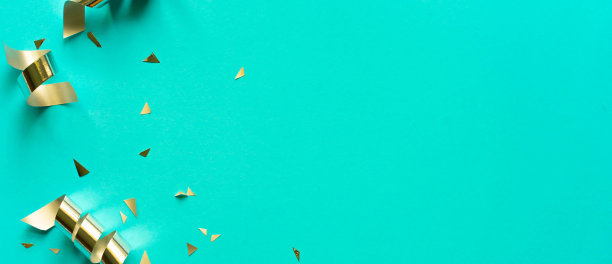 近距离拍摄一组金色的滚动彩带和五彩纸屑，在蓝绿色的背景上复制空间，为圣诞节快乐新年，嘉年华，生日和周年，概念设计图片下载