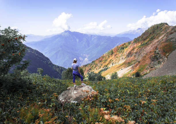 年轻女子从后面站在大山中间的大石头上图片下载