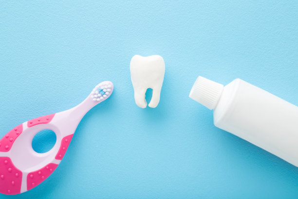 白色牙齿，牙膏管和粉红色牙刷在浅蓝色的桌子背景。柔和的颜色。婴儿牙齿卫生。特写镜头。自顶向下的观点。图片下载