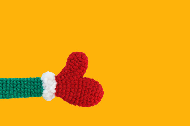 一个编织玩具红色手套绿色袖子白色袖口显示右拇指向上黄色背景，孤立图片下载