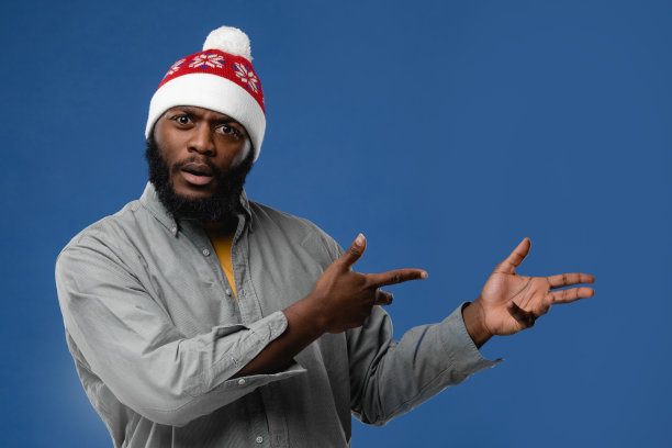 戴着圣诞帽的非裔美国年轻人的肖像。概念照片在工作室的彩色背景图片下载