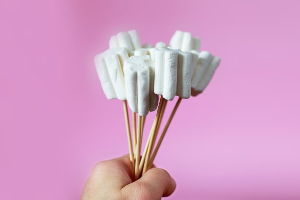 粉红色背景上的棉花糖花束。孩子的手拿着一束糖果图片下载