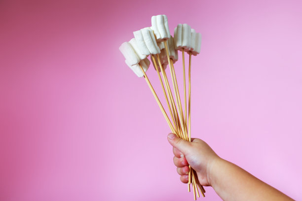 粉红色背景上的棉花糖花束。孩子的手拿着一束糖果图片下载