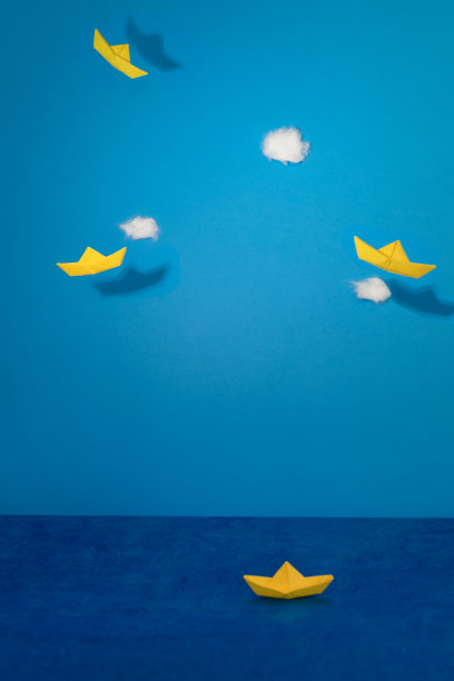 折纸的黄色帆船在蓝色的纸天空中飞翔。图片下载