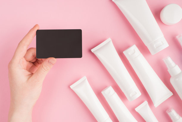 化妆品店代金券概念。上面的头顶pov第一人称查看照片的女性手握代金券孤立在粉红色柔和的背景与白色奶油管图片下载