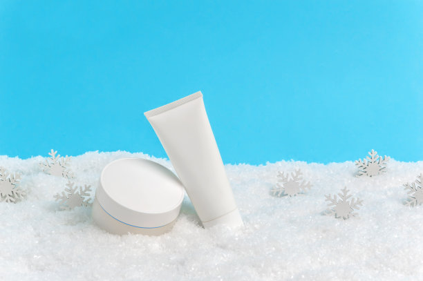 面霜瓶和护手霜或身体乳管在雪在蓝色的背景。冬季护肤化妆品。季节性寒冷天气保护皮肤图片下载