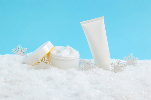 面霜瓶和护手霜或身体乳管在雪在蓝色的背景。冬季护肤化妆品。季节性寒冷天气保护皮肤图片下载