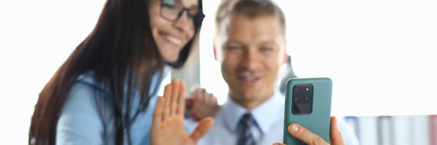 在智能手机上，男人和女人微笑着向对话者挥手致意图片下载