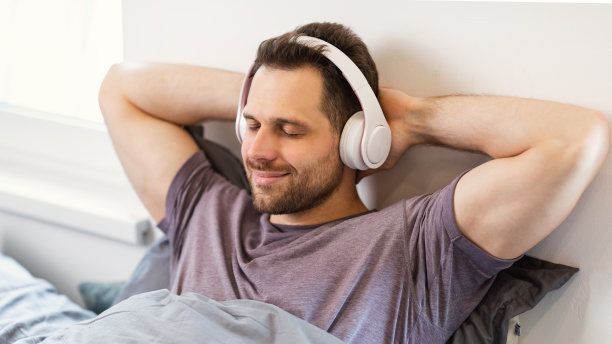 在家的床上戴着耳机听音乐的放松男人图片下载