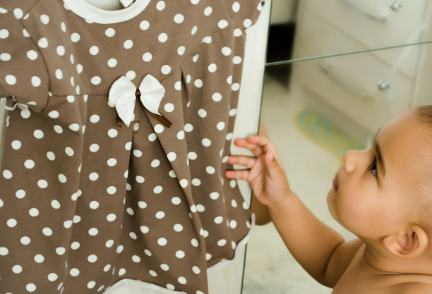 可爱的小女孩看着带白点的棕色连衣裙。图片下载