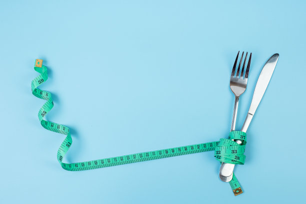 俯视图绿色卷尺绕叉子和刀在蓝色背景。节食、减肥、肥胖和食物控制的概念图片下载
