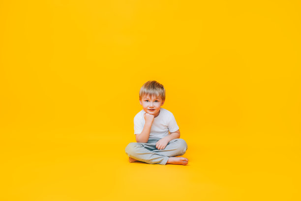 穿着白色t恤坐在黄色背景上沉思的小男孩图片下载