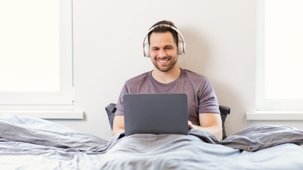 男人用笔记本电脑，戴着耳机坐在卧室看电影图片下载
