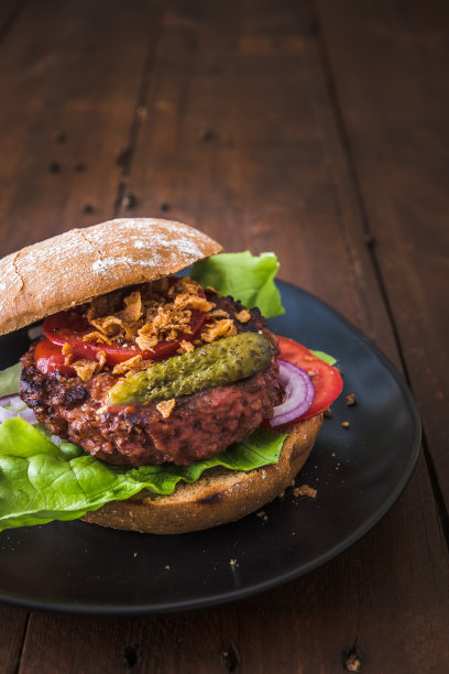 汉堡配素食汉堡肉饼，沙拉，西红柿和烤洋葱放在一个黑色的盘子上，放在木桌上，竖直的库存照片和拷贝空间图片下载