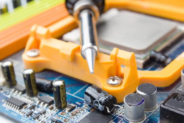 电烙铁在电脑板的背景和电容器的软焦点。图片下载