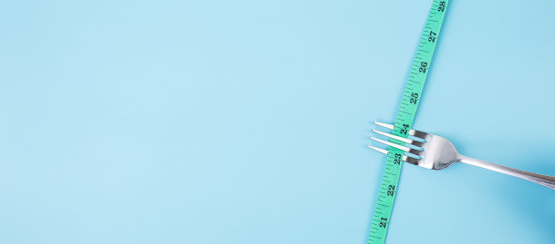 俯视图绿色卷尺绕叉子和刀在蓝色背景。节食、减肥、肥胖和食物控制的概念图片下载