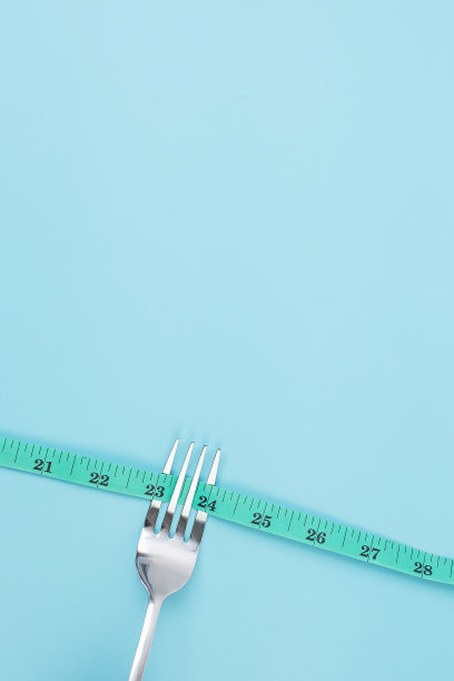 俯视图绿色卷尺绕叉子和刀在蓝色背景。节食、减肥、肥胖和食物控制的概念图片下载