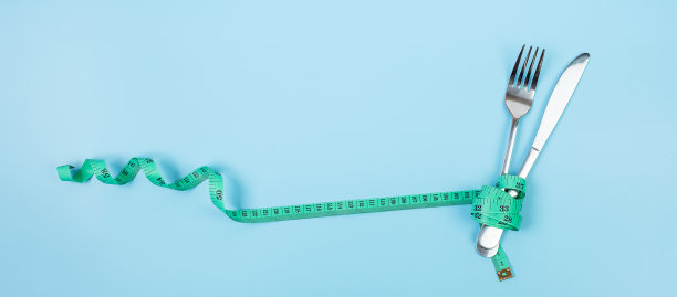 俯视图绿色卷尺绕叉子和刀在蓝色背景。节食、减肥、肥胖和食物控制的概念图片下载