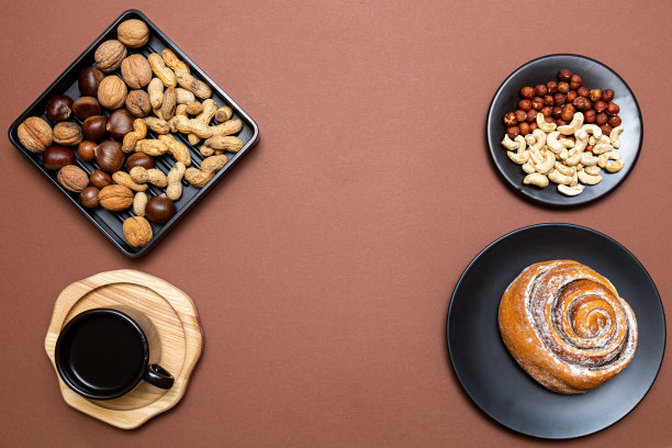 健康的早餐，肉桂面包，腰果，榛子，核桃，栗子和花生在黑色的盘子和一杯黑咖啡在棕色的背景。文本。图片下载