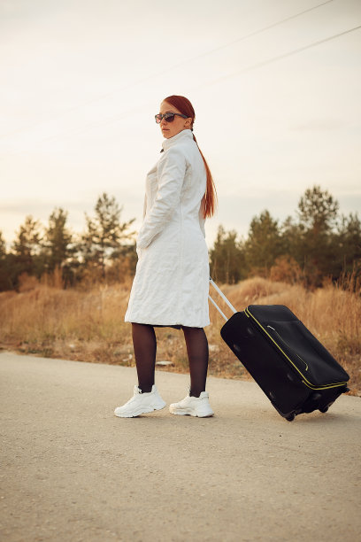 一个孤独的女人提着行李箱走在空荡荡的路上，旅行的概念，要在一个未知的地方独自一人。图片下载