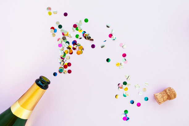香槟瓶与明亮的五彩纸屑在粉红色的背景，平铺。具有复制空间的创意假日构图图片下载