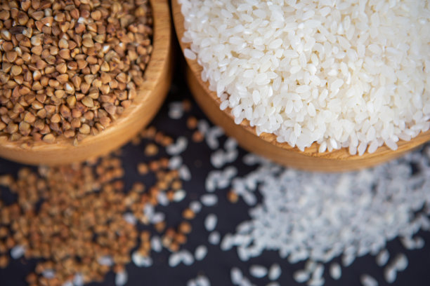 米和荞麦在美丽的木杯在黑色的背景。图片下载