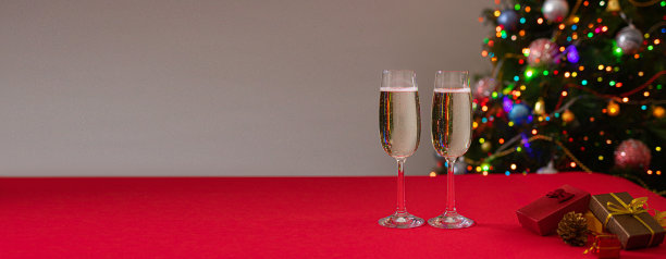新年照片眼镜放在红色的桌子上，香槟酒在背景上的圣诞树与灯和侧面。假日和牛年。横幅图片下载