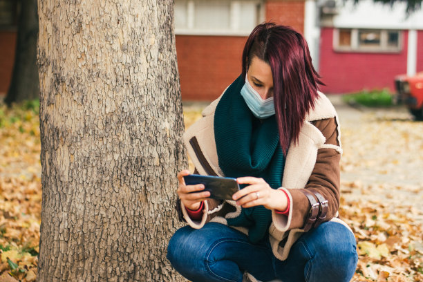 女人戴着面具，用智能手机拍摄街头库存照片图片下载