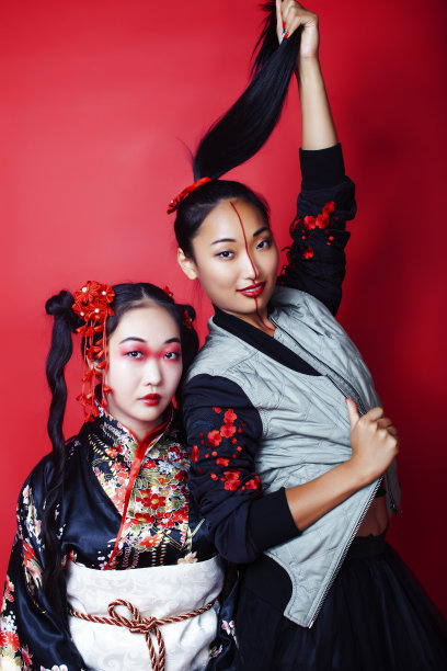 两个漂亮的艺伎女孩朋友:现代亚洲妇女和传统穿着和服摆出欢快的红色背景图片下载