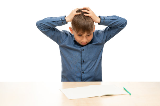坐在桌旁的孩子用双手抓住他的头。儿童肖像孤立在白色背景。图片下载