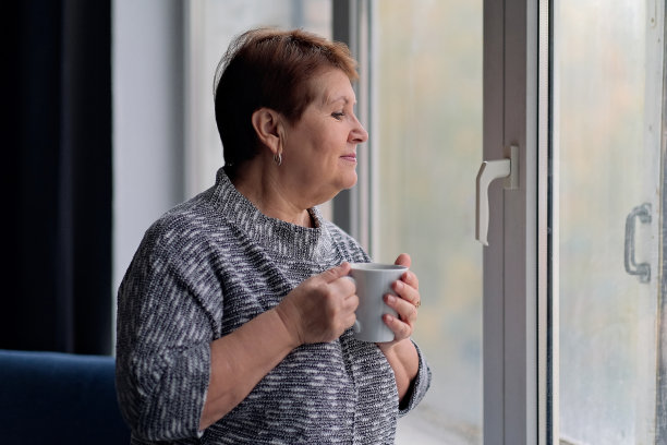 年长妇女的肖像与一杯咖啡看着窗外。优雅成熟的女士喝热咖啡和放松靠近窗口微笑和梦想室内图片下载