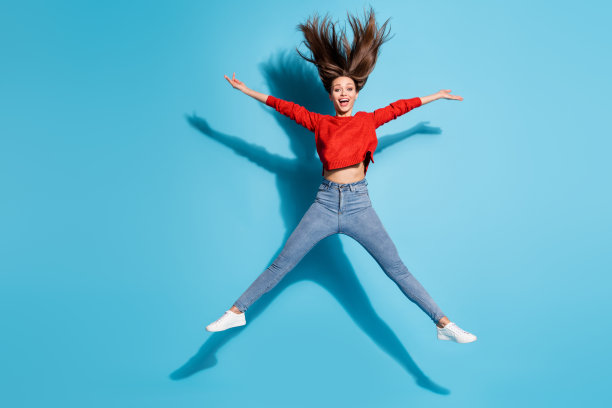 全身照片疯狂的女士跳起来展开胳膊腿头发飞扬穿红色毛衣运动鞋牛仔裤孤立的蓝色背景图片下载