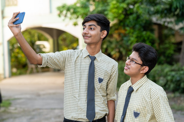 男学生在校园里使用智能手机自拍。图片下载