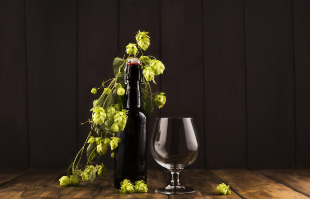 手工啤酒瓶在黑玻璃和空玻璃。木质背景上放着酒精饮料和新鲜的啤酒花。副本的空间。高质量的照片图片下载
