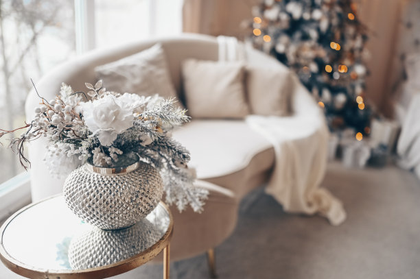 新年的花束装在银花瓶里放在沙发旁边的玻璃桌子上，装饰着圣诞树图片下载