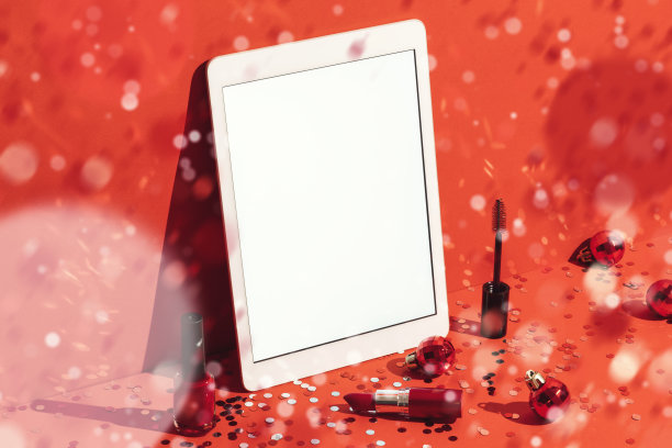 数字平板模型，模板和化妆品在红色背景与五彩纸屑雨图片下载