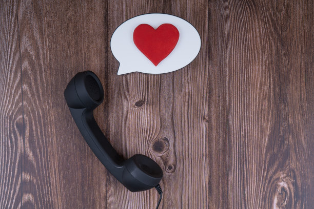 电话接收器与气球泡沫和红心木制背景。图片下载