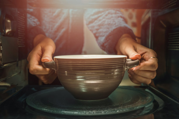 女人的手从微波炉里拿盘子，从里面拍照。照片与照明图片下载