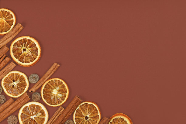 季节性的平铺在角落里的自然干橘子片，肉桂棒和橡子帽在棕色的背景图片下载