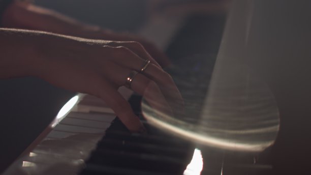一位女钢琴家在一架漂亮的大钢琴上弹奏着轻柔的古典音乐，特写慢动作。钢琴琴键用深色拉近。前景中来自光线和烟雾的眩光图片下载