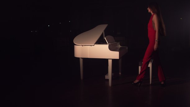 一个穿着红裙子的年轻漂亮的女孩走到白色的钢琴前坐下。古典音乐的康奈特。大厅里弥漫着浪漫的气氛图片下载