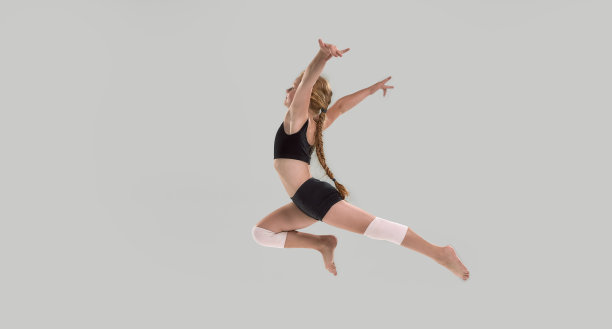 长镜头可爱的小红发女孩，专业体操运动员跳过灰色背景孤立图片下载