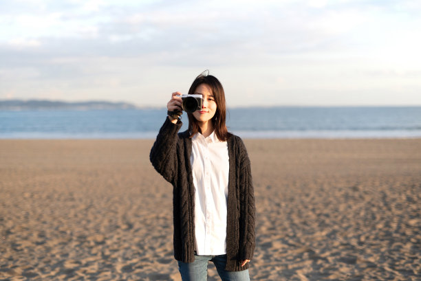 年轻的女游客在海滩上拍照黄昏图片下载